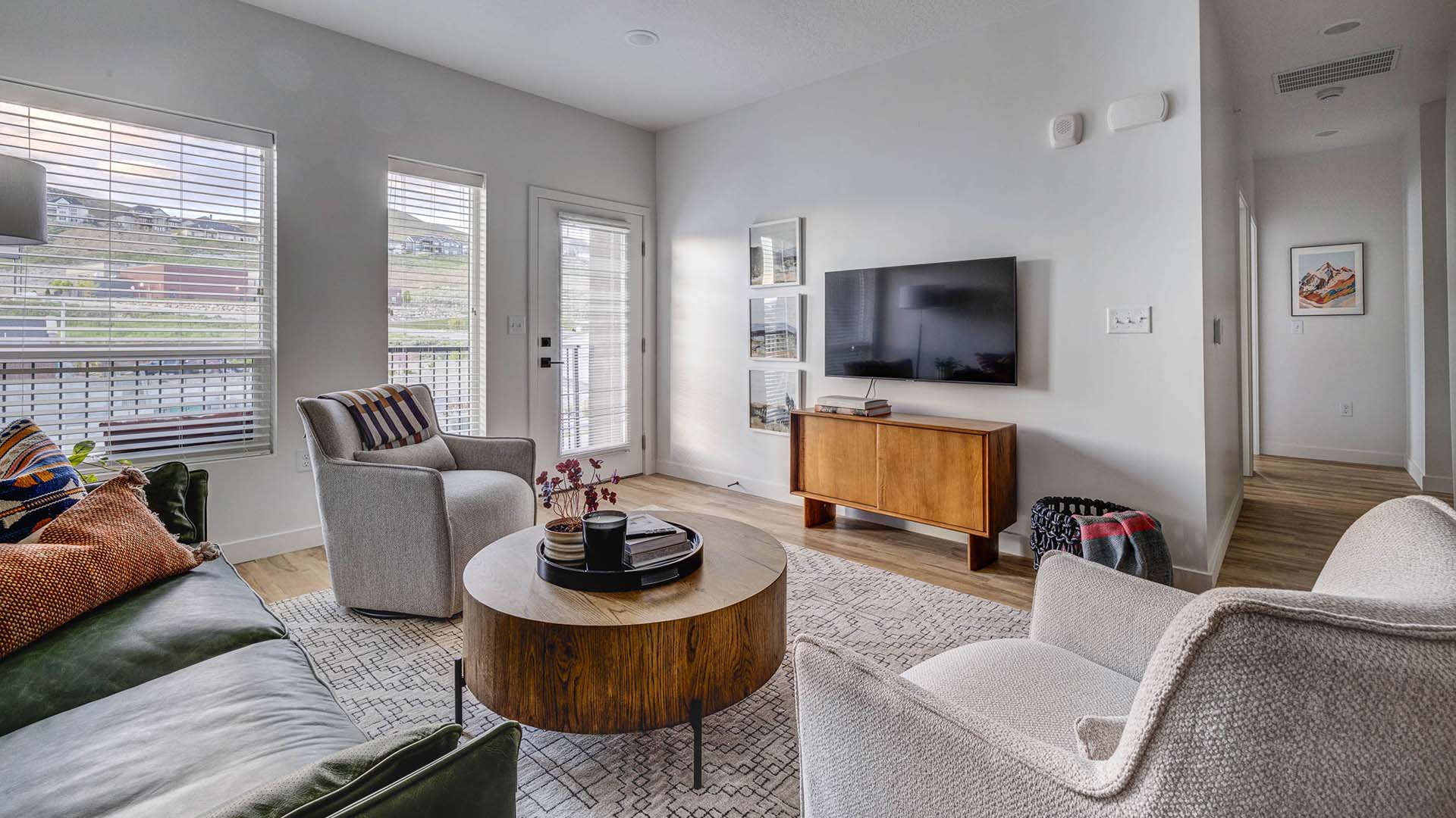 Apartment living room with large rug, plush seating, round coffee table, TV, and door to balcony.