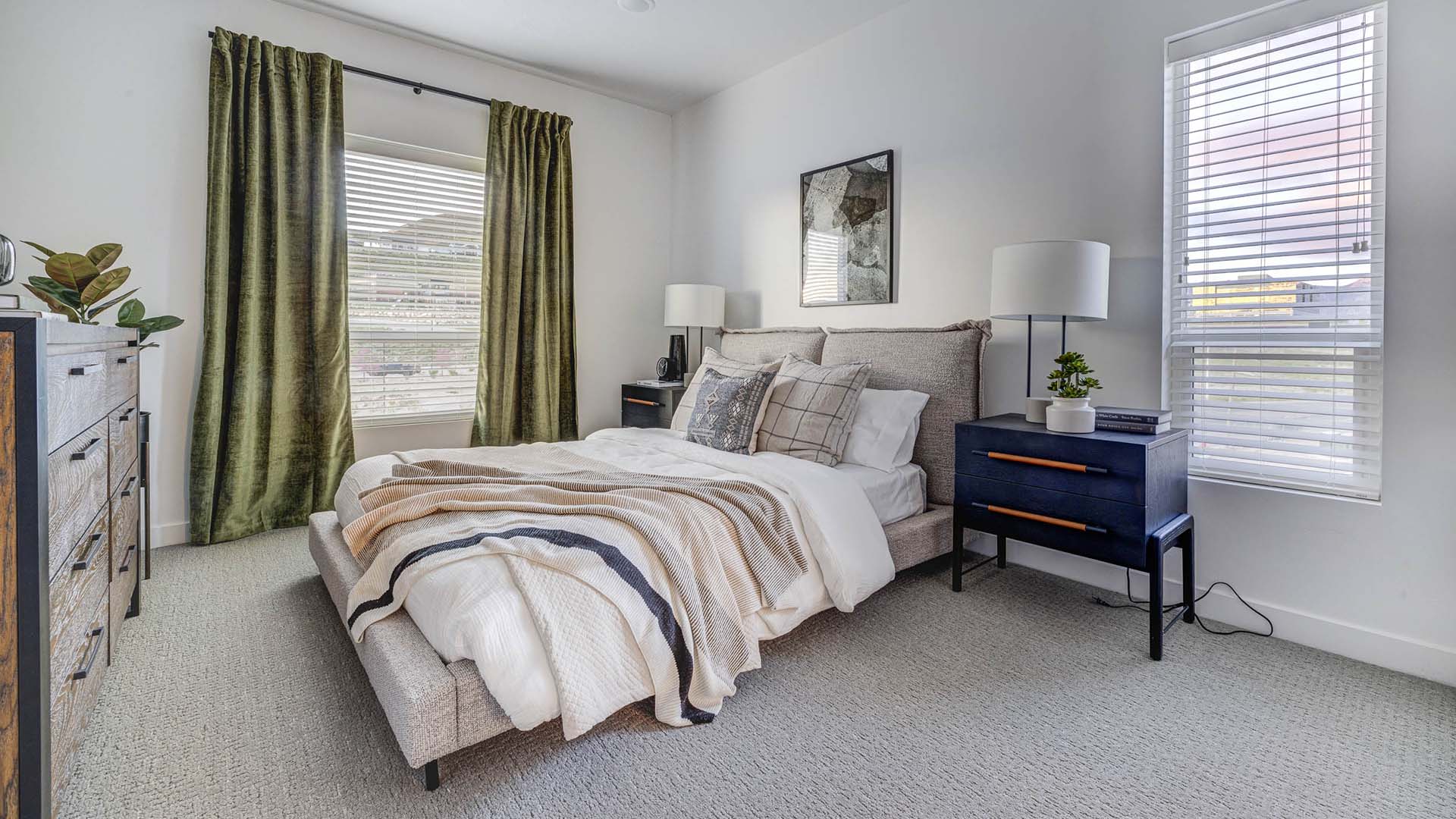 Bedroom with carpet, plush bed with headboard, bedside drawers with lamps, and large windows.