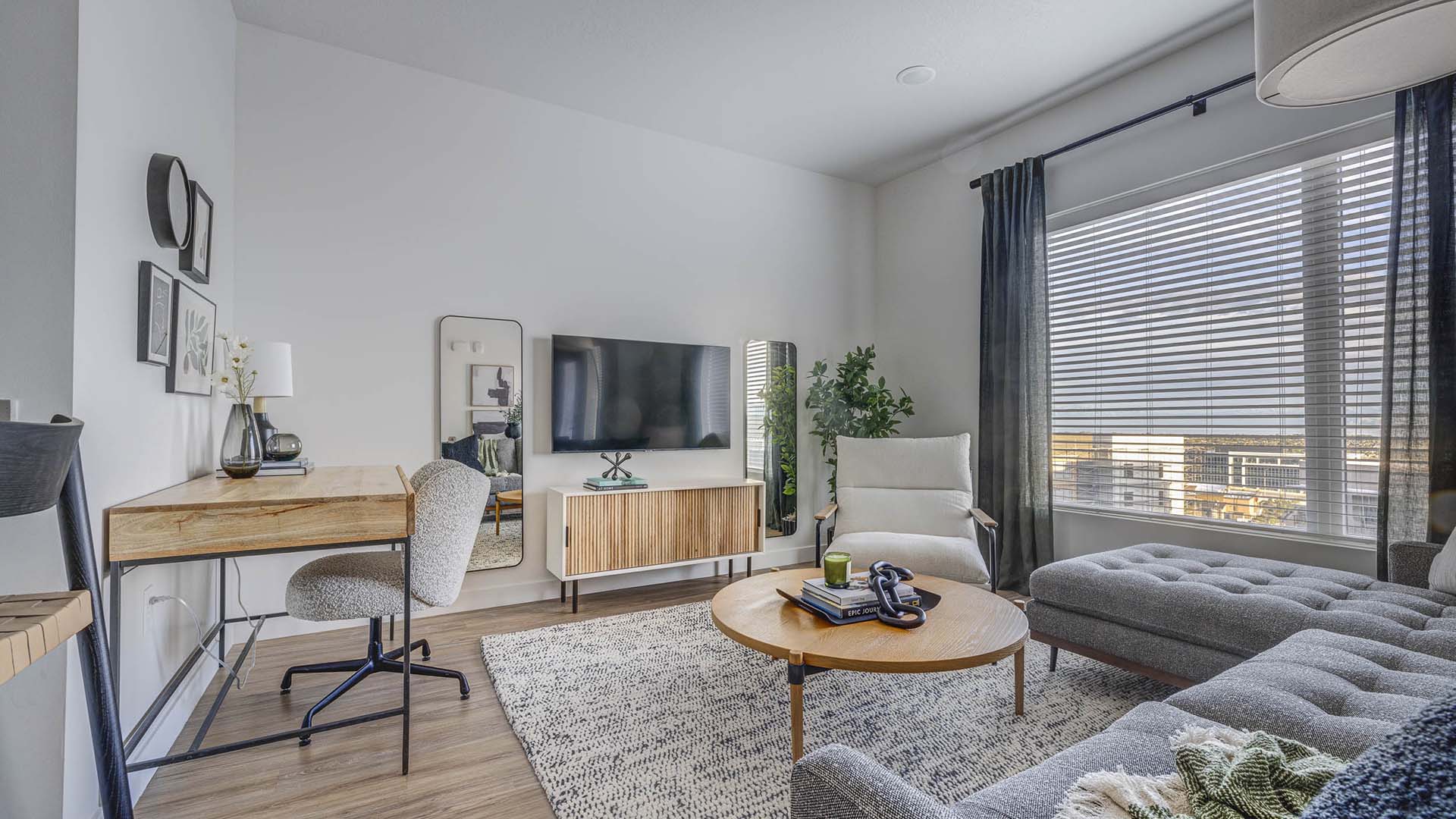 Apartment living room with large rug, plush couch, desk with decor, TV, and large window.