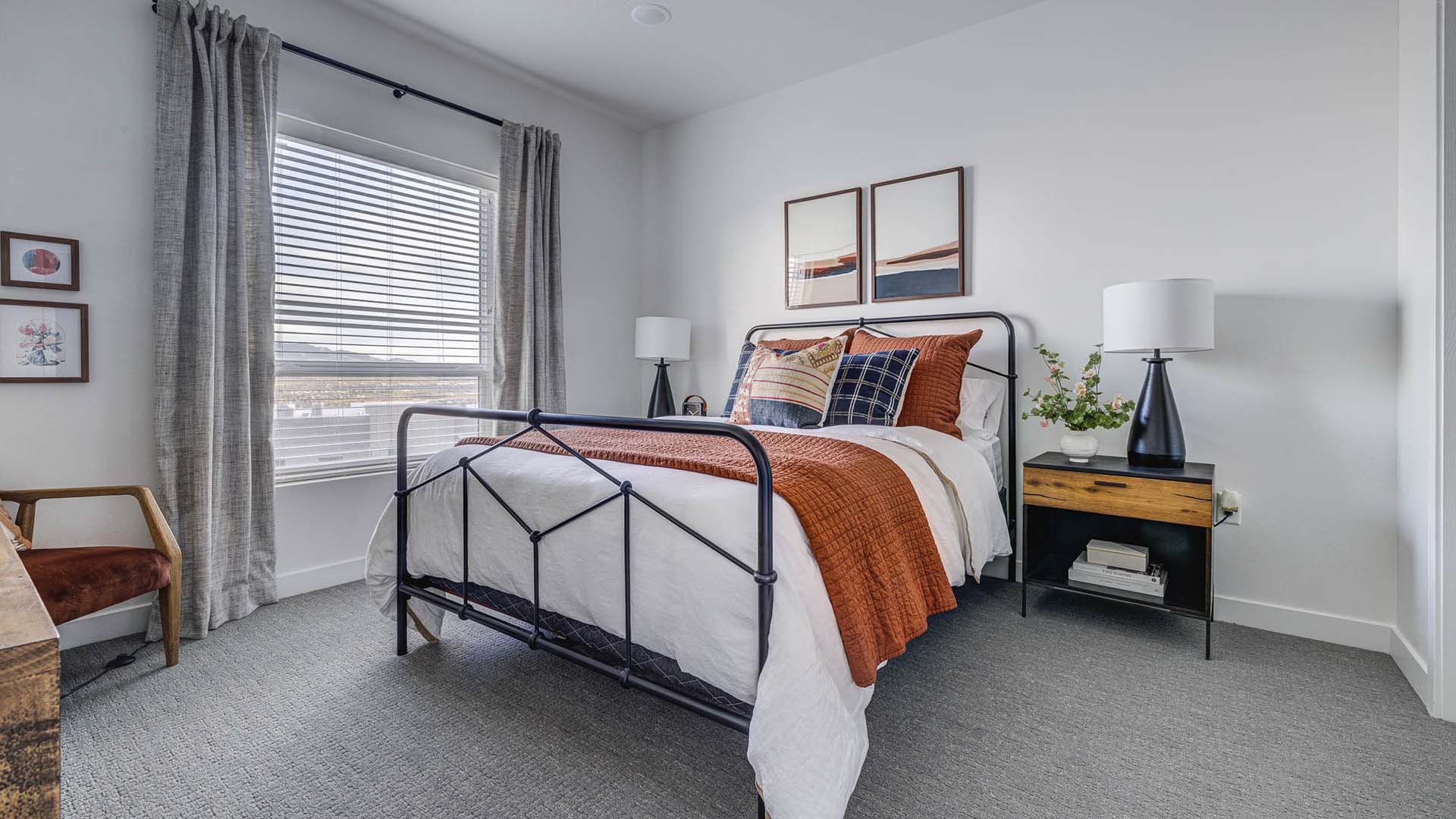 Bedroom with carpet, metal bed frame with plush bedding, bedside drawers with lamps, and large window.
